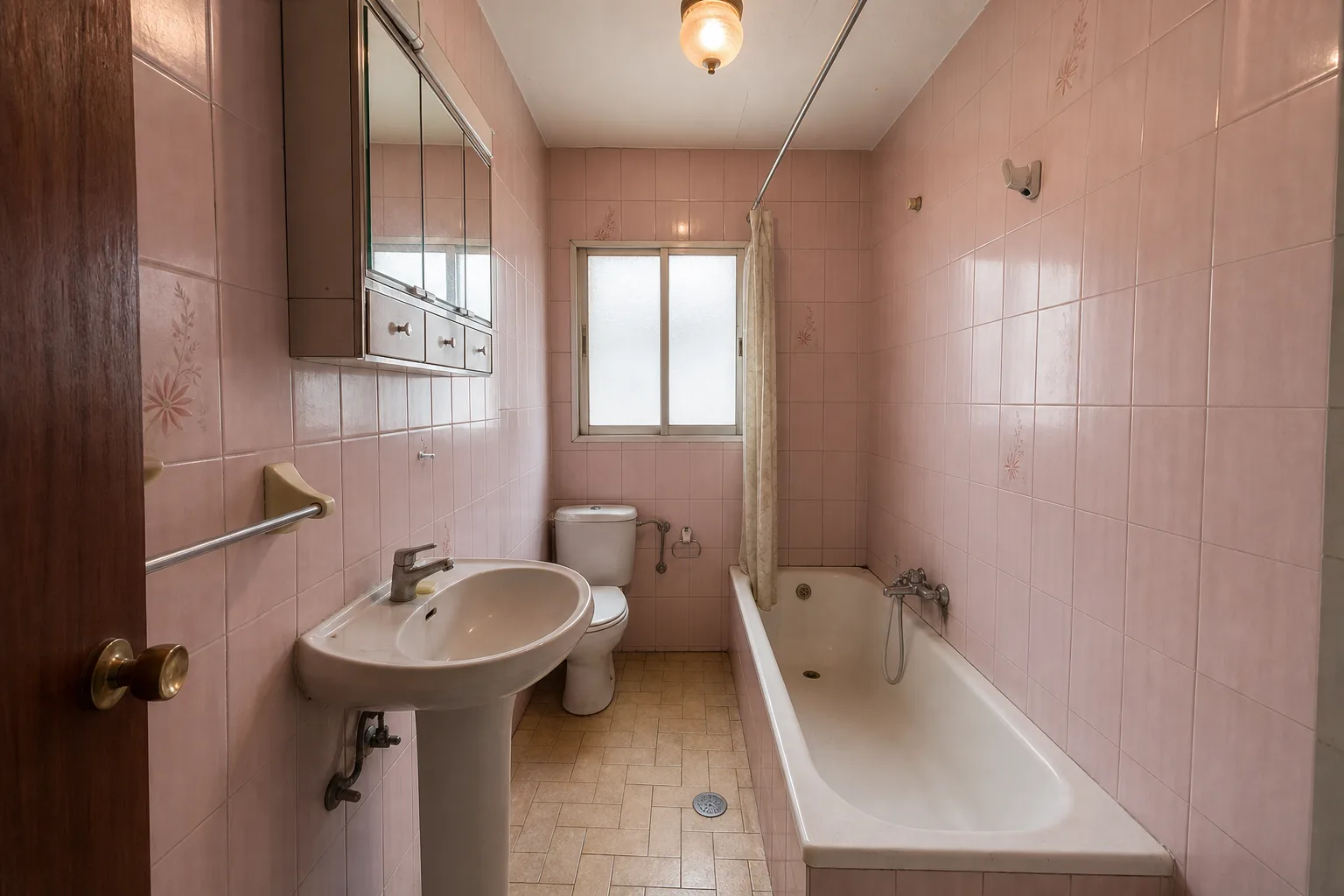 Baño estrecho antiguo con azulejos rosas, bañera y lavabo de pedestal